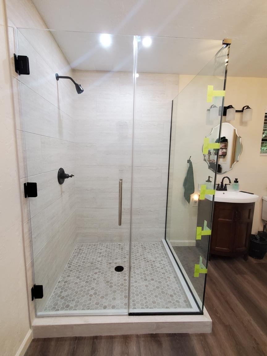 Glass shower door installation in progress with yellow tape securing the glass panels in a tiled bathroom.