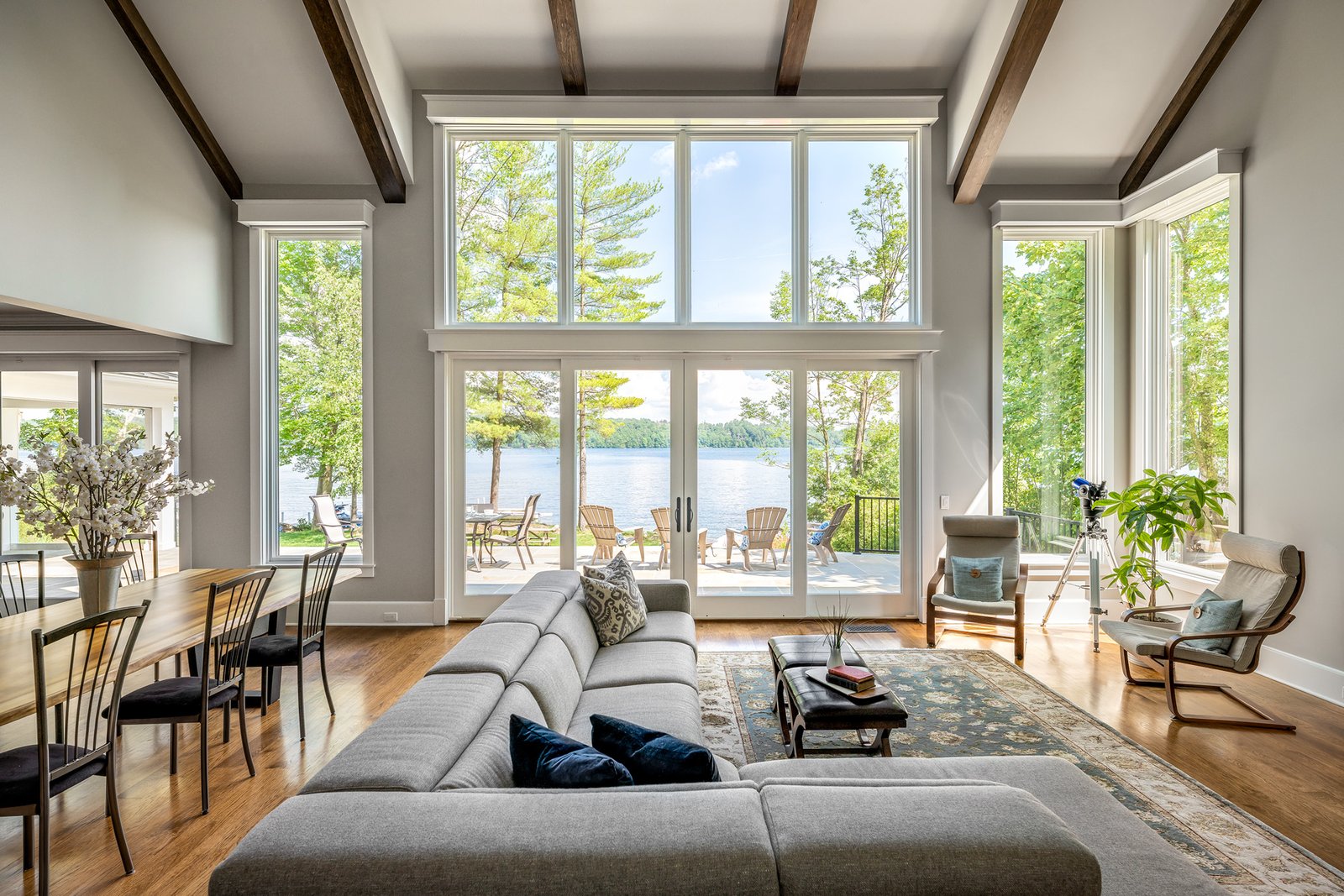 Large residential windows and glass patio doors in a living room overlooking a lake with outdoor seating on a deck