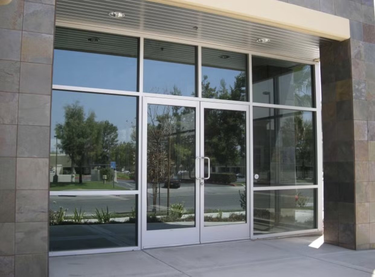 Aluminum framed glass double entry doors with surrounding storefront windows on a commercial building exterior.
